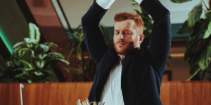 A man in a suit is doing yoga in front of his laptop.